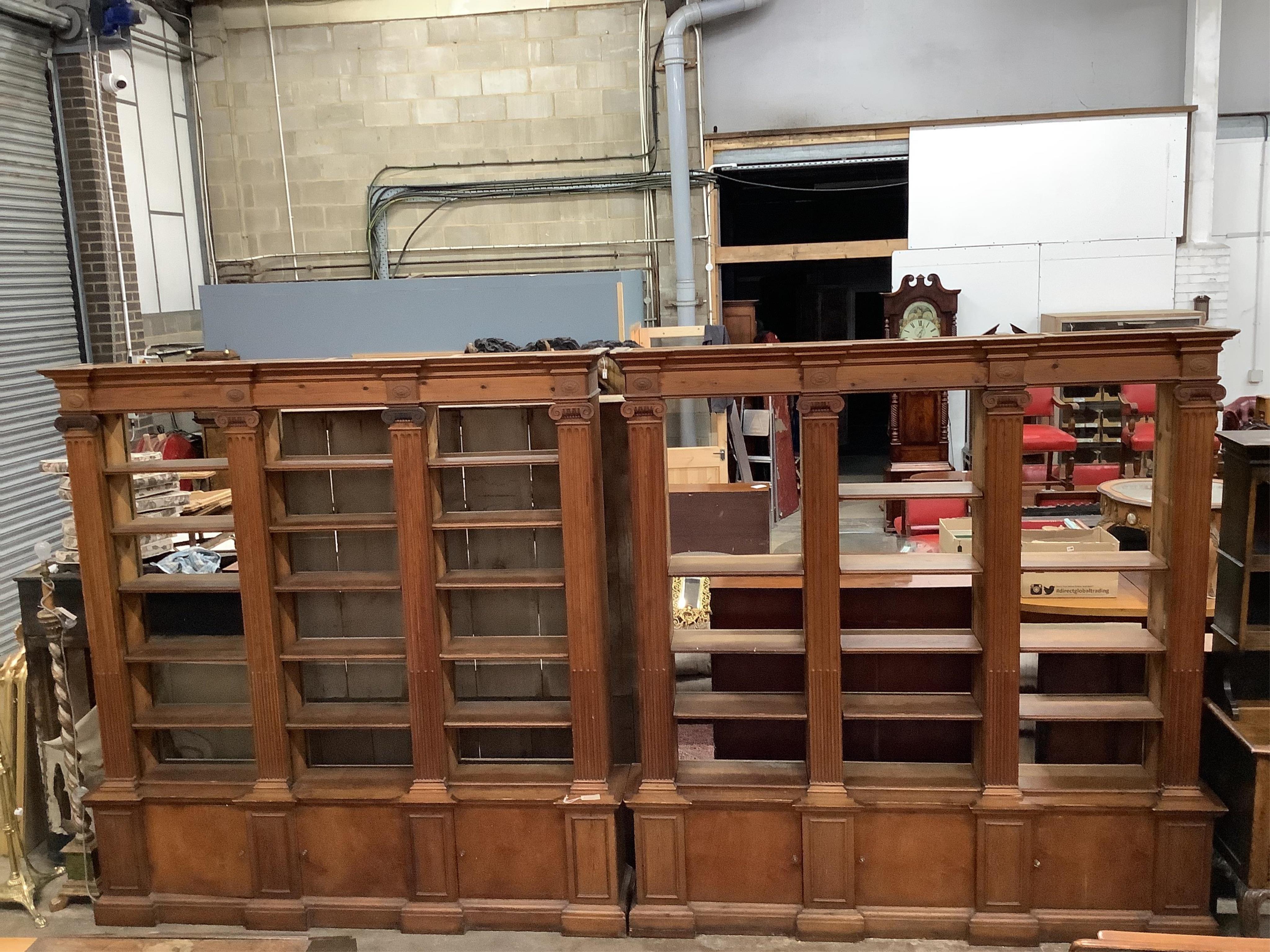 A pair of mid 20th century Sheraton style pitch pine and ply open bookcases, the adjustable shelves divided by fluted Ionic columns, each width 214cm, depth 33cm, height 222cm
